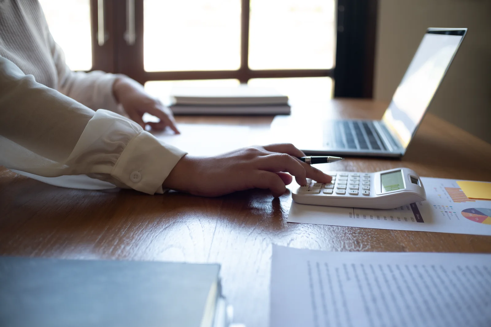 Accountant working through paperwork at a desk with a laptop and calculator